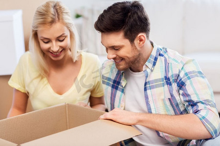 抵押贷款，搬家和房地产概念—快乐的夫妇看里面的盒子或包裹在家里。快乐的夫妇看里面的盒子或包裹在家里