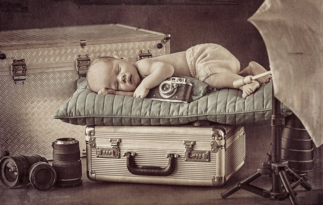 行李箱男孩摄影照片_睡在银色行李箱上的可爱小摄影师