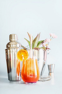 黄色橙色长饮料，配冰块和玻璃杯中的橙色水果切片。餐桌上有鸡尾酒、酒吧用具，背景明亮，有复印空间。