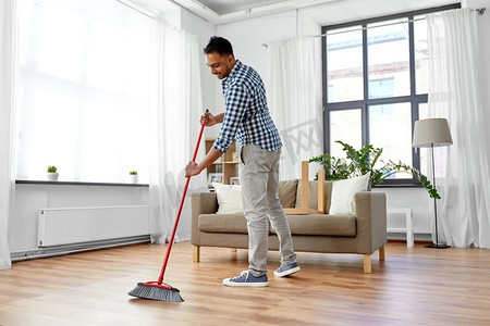 扫地男人摄影照片_清洁、家务和家政概念--印度男人在家里扫地。家里拿着扫帚打扫地板的男人