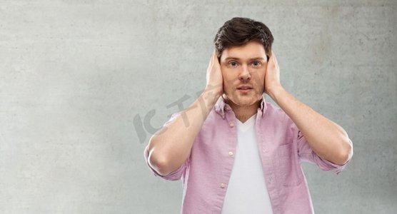人，噪音和压力概念—男子关闭耳朵的手在灰色背景。一名男子在灰色混凝土墙上用手捂住耳朵