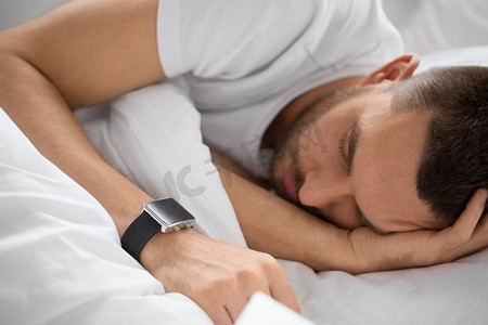 人、科技、休息理念--带着智能手表睡在床上的男人特写。带着智能手表睡在床上的男人的特写