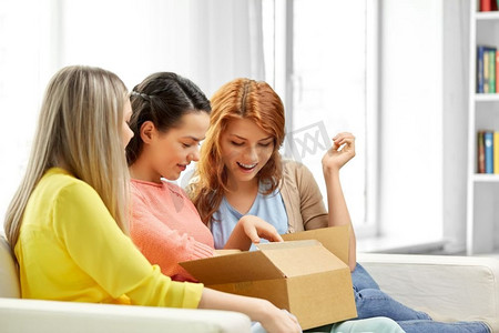 快递和友谊的概念-三个十几岁的女孩或朋友在家里打开包裹盒子。十几岁的女孩或朋友打开包裹盒子