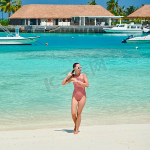 穿着连体式泳衣的女子在白色沙滩上行走。在马尔代夫度暑假。