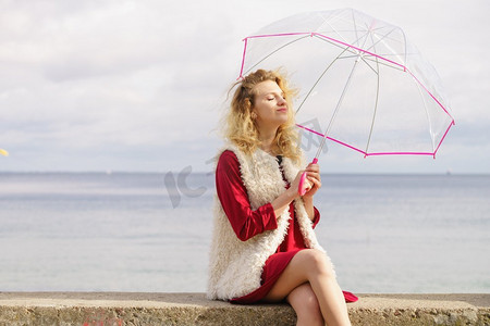 透明的伞摄影照片_愉快优雅的成年妇女拿着透明伞反对天空。天气预报概念快乐的女人撑伞