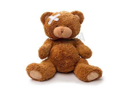 医学、保健和儿童概念-白色背景下头上有医疗贴片的泰迪熊玩具。头上贴着医疗贴片的泰迪熊玩具