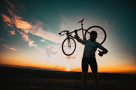 骑自行车的silhoutte与自行车提高到天空比赛和胜利概念