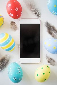 复活节、节日和物体概念-白色背景上彩色彩蛋和羽毛的特写。带有复活节彩蛋和羽毛的智能手机