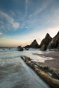 Westcombe海滩美丽的日落风景图象在德文郡英格兰与锯齿状岩石在海滩和惊人的云形成