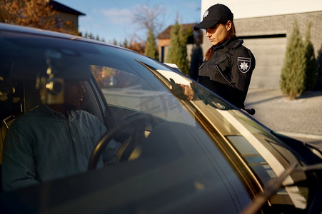 年轻的女警察与平板电脑站在汽车附近。女交警在路上工作。年轻的女警察与平板电脑站在汽车附近