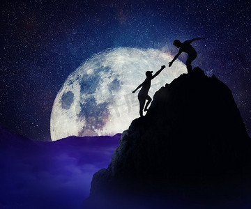 一名男子向朋友伸出援手，帮助他们攀登山岩悬崖。团队合作精神和在危险情况下的信任观念。满月之夜的背景。