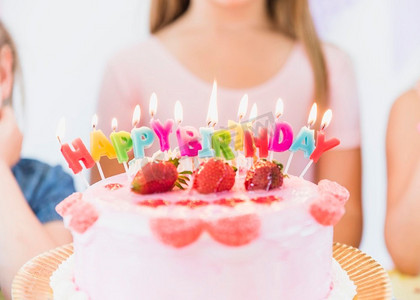 蛋糕周年摄影照片_关闭五颜六色的发光生日蜡烛草莓浇头蛋糕