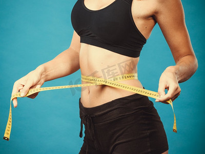 减肥，苗条身材，健康生活理念。适合健身女孩测量她的腰围与测量磁带在蓝色