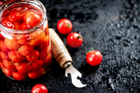 在桌子上的玻璃瓶里腌制的西红柿。在黑色背景上。高质量的照片。在桌子上的玻璃瓶里腌制的西红柿。