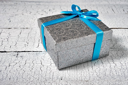 礼物生日圣诞节礼物概念—银礼品盒与蓝色丝带在白色被画的木背景。俯视图。蓝丝带礼盒