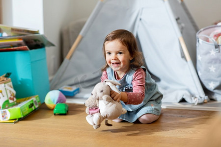 童年，休闲和人的概念—快乐的小女婴在家里玩软玩具。快乐的女婴玩软玩具在家里