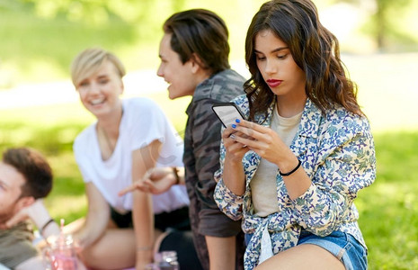 休闲、科技和人的概念-女性在夏令营与朋友野餐时使用智能手机。与朋友野餐时使用智能手机的女性