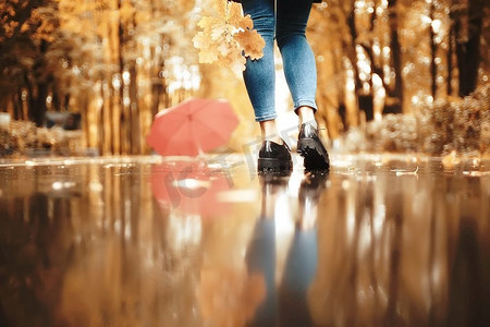 秋天风景在公园有一把红伞的女孩/概念秋天天气下雨，一个年轻的妇女在伞下