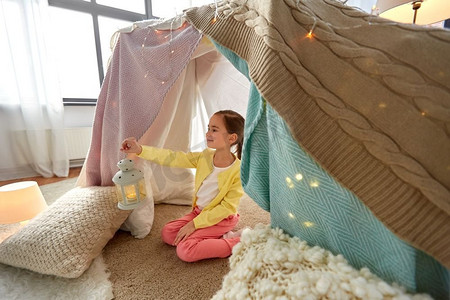 teepee摄影照片_童年和hygge概念—有灯笼的快乐的小女孩在孩子帐篷或帐篷在家里小女孩与灯笼在孩子们帐篷在家里