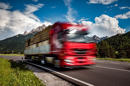 一辆运木材的卡车在阿尔卑斯山的背景下疾驰而下.卡车在移动模糊。