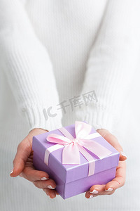 女性手持带有粉色丝带的紫色礼品盒。手拉手礼品盒
