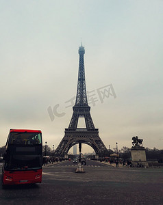 一辆红色旅游巴士在巴黎著名地标埃菲尔铁塔前的人行道上行驶，从街上可以看到。