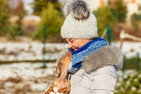 年轻女子在外面的雪地里玩得很开心。一只母狗在寒冷的冬日和她的纯种小狗玩耍。一名女子在冬天与狗玩耍