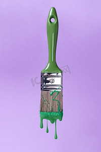 刷与绿色油漆，油漆滴从刷子滴在紫色的背景。刷上绿色油漆，