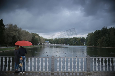雨在秋天公园/年轻的25岁夫妇男人和女人走在伞下在潮湿的雨天，走十月情人