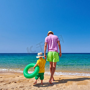 两岁的蹒跚学步的男孩在海滩上与父亲走，拿着充气戒指。暑假家庭度假。希腊，西托尼亚。 