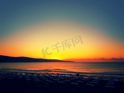 太阳伞摄影照片_金色的日落落在海滩上，挂满了太阳伞。晴朗的天空，平静的大海。