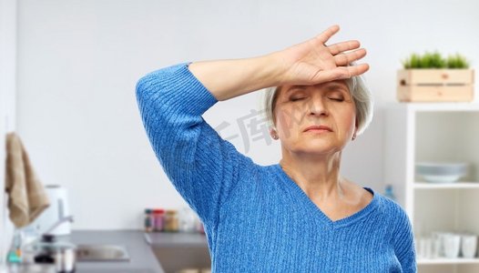 疲惫背景摄影照片_健康，压力和老年人概念—疲惫的老年妇女遭受头痛的家庭厨房背景。疲惫的高级妇女在厨房