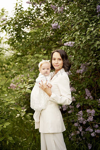 花园里年轻漂亮的妈妈和可爱的小女儿的户外时尚写真。丁香花。春光映象