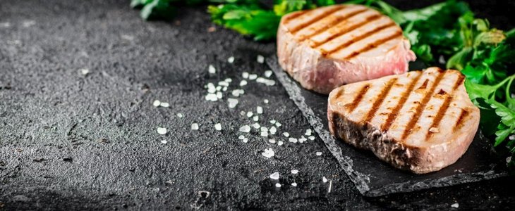 烤金枪鱼与欧芹和盐的石头板。黑色背景。高质量的照片。烤金枪鱼与欧芹和盐的石头板。 
