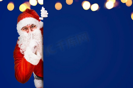 圣诞老人用手指在嘴唇上要求安静与彩色广告板和复制空间。圣诞老人要求安静