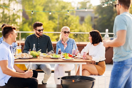 休闲和人的概念快乐的朋友在夏天在屋顶上举行烧烤派对。快乐的朋友在屋顶上举行烧烤派对