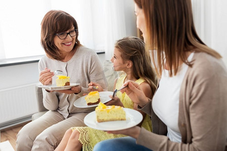 家庭、世代和食物概念—微笑的母亲、女儿和祖母在家里吃蛋糕。母亲，女儿和祖母吃蛋糕