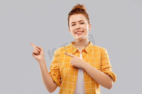 和人的概念-微笑的红头发少女穿着格子衬衫指着灰色背景上留下的手指