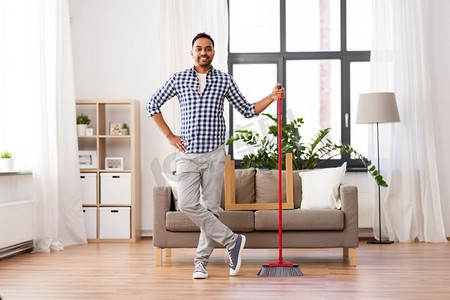 清洁、家务和家政概念--微笑的印度男人，家里拿着扫帚。微笑的印度男子在家里打扫扫帚