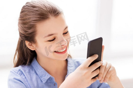 儿童，技术和通信概念—微笑的女孩消息在智能手机在家里。微笑的女孩消息在智能手机在家里