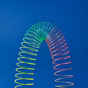 在蓝色背景和复制空间上层叠抛物线形状的五颜六色的玩具螺旋。蓝色背景上的柔性塑料彩虹弹簧。