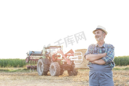 微笑的农民站在与手臂交叉反对收割机在农场