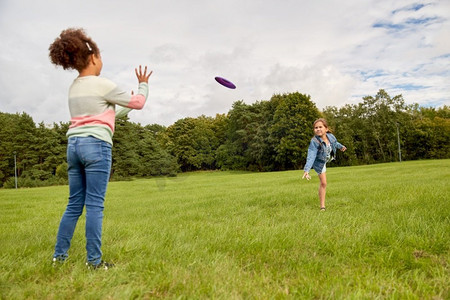 游戏金子摄影照片_童年、休闲和人的概念快乐的女孩在公园玩飞盘游戏。快乐女孩在公园玩飞碟