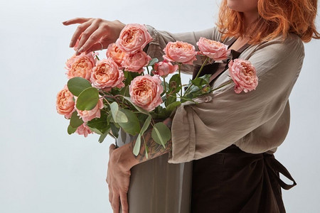 花瓶里的粉红玫瑰。一个年轻的红头发女孩拿着一瓶花。鲜花店概念一个红头发的女孩拿着一束玫瑰花花瓶