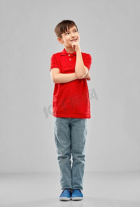童年，表情和人的概念--穿着红色马球衫的小男孩在灰色的背景下思考。穿着红色马球T恤的会思考的男孩