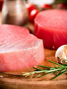 新鲜的生金枪鱼牛排配迷迭香和大蒜。背景是质朴的。高质量的照片。新鲜的生金枪鱼牛排配迷迭香和大蒜。
