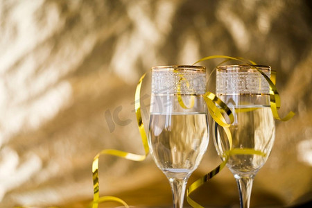 透明飘带摄影照片_模糊背景下的金色飘带透明香槟酒杯