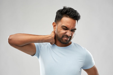 健康问题和人的概念—不健康的印度男子遭受脖子疼痛在灰色背景。不健康的印度男子遭受颈部疼痛