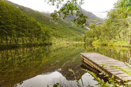 夏天湖边的老木头码头，宁静的挪威风景，背景是群山。夏天湖塘上的老木墩