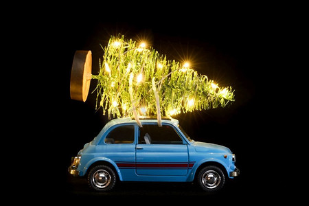 蓝色复古玩具汽车交付圣诞节或新年照明树在黑色背景。汽车送圣诞树或新年树